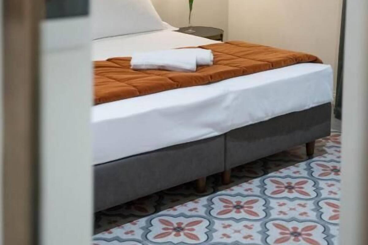 A hotel room with a bed, a nightstand, a wall-mounted light, and a patterned floor.