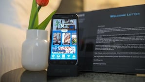 A smartphone displaying a travel app interface with a welcome letter and a vase with a red tulip.