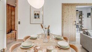 Un comedor con una mesa redonda para seis personas, una puerta de madera y una lámpara colgante moderna.
