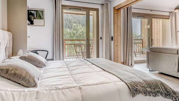 Un dormitorio con una cama grande, un sofá y un balcón con vistas a árboles.