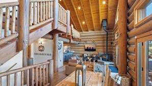 A log cabin interior with a wooden staircase, a fireplace, and a cozy seating area.