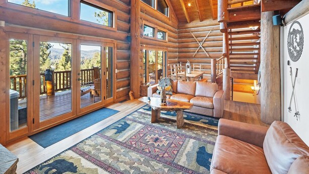 A log cabin interior with a large living area, a staircase, and a view of the outdoors.