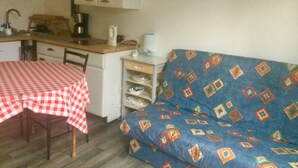 Ett kompakt kök med ett matbord täckt av en röd- och vitrutig duk, en blå soffa med ett mönstrat överdrag och ett vitt skåp ovanför bänkskivan.