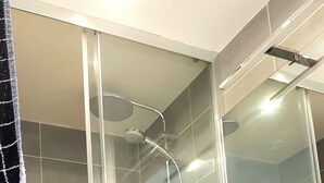 Ett badrum med en dusch som är avskärmad med glasväggar, ett handfat i trä med en spegel och kaklade väggar.