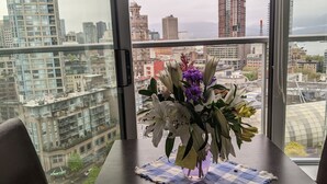 A table with a vase of flowers and a placemat in a high-rise room with a city view. - Ocean, Mountain, City Views, Fully Furnished, Downtown Vancouver (Vancouver)