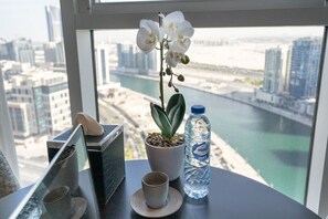 Une table sur laquelle se trouvent un pot d’orchidée, une bouteille d’eau et une tasse, avec une vue sur le paysage urbain par la fenêtre.