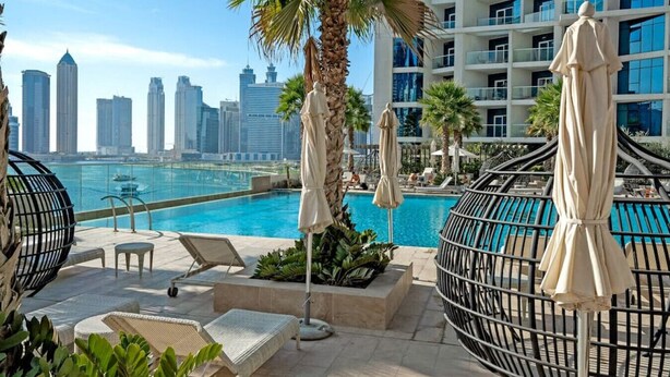 Un área de piscina en la azotea con sillones de descanso, sombrillas y vistas al horizonte de la ciudad.