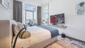 Habitación de hotel con cama, escritorio, silla, televisor y ventana con cortinas.