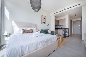 A modern bedroom with a large bed, a green sofa, and a kitchen area in the background.