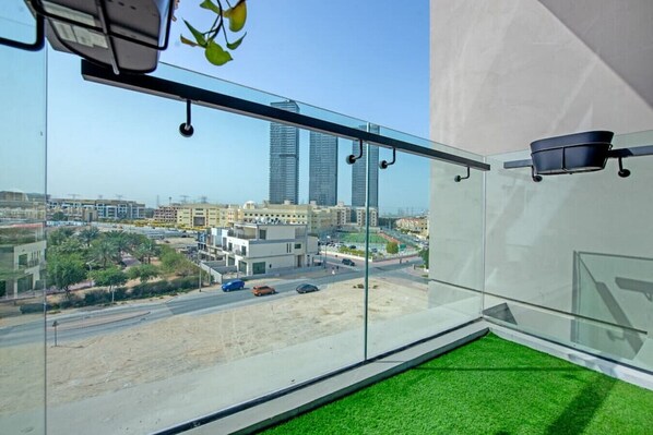 Una habitación moderna con balcón de cristal, vistas a un paisaje urbano y suelo de césped artificial verde.