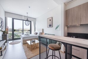 A modern kitchen with a bar area, a dining space, and a bedroom with a large window.
