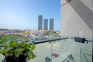 Ein Balkon mit Blick auf zwei hohe Gebäude, einen Parkplatz und einen Blumentopf.