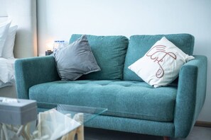 Ein blaugrünes Sofa mit zwei Kissen, eines grau und eines weiß mit einem Muster.