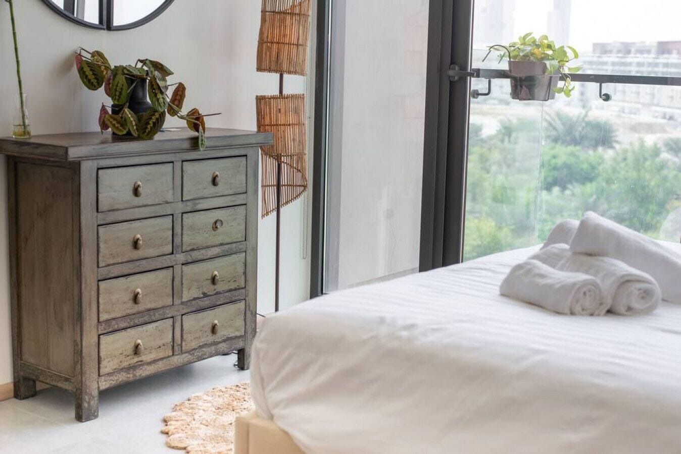 A bedroom with a bed, a dresser, and a view of greenery outside.