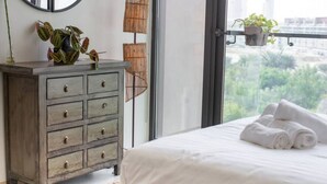 A bedroom with a bed, a dresser, and a view of greenery outside.