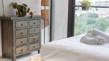 A bedroom with a bed, a dresser, and a view of greenery outside.