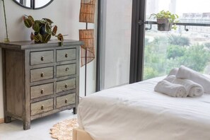 A bedroom with a bed, a dresser, and a view of greenery outside.