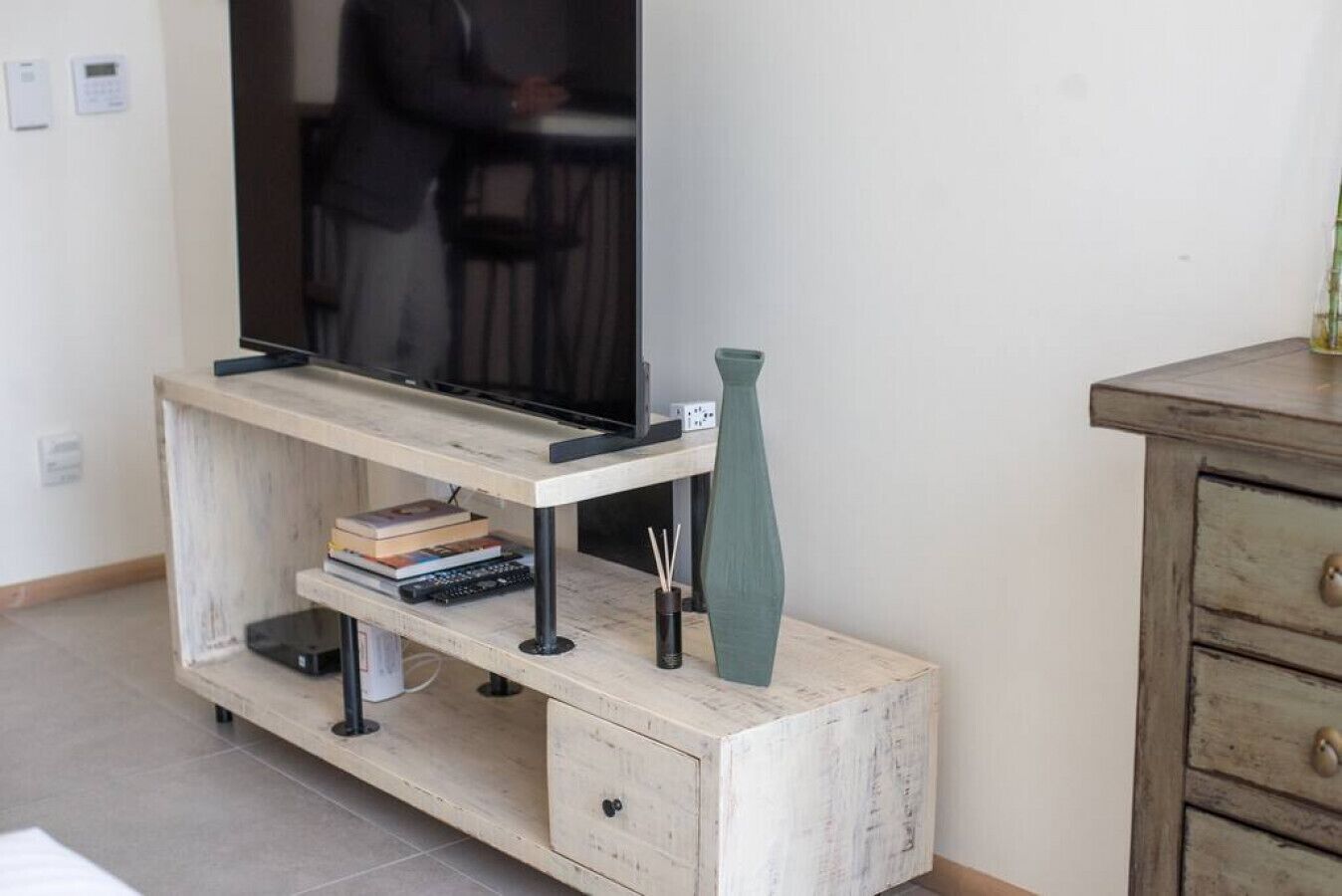 A wooden TV stand with a flat-screen TV, a vase, and books.