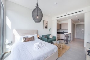Et moderne soveværelse med en stor seng, en grøn sofa, et spiseområde og et køkken i baggrunden.