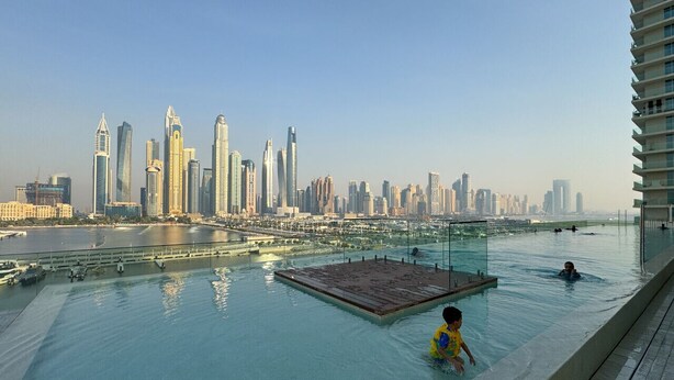 Ein Infinity-Pool auf dem Dach mit Blick auf die Stadtlandschaft, einer großzügigen Sonnenterrasse und einem Hochhaus am rechten Rand.