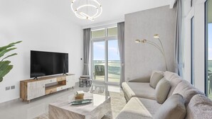 Ein modernes Wohnzimmer mit Flachbildfernseher, Holzkonsole, Marmortisch, beiges Sofa und einem großen Fenster mit Blick ins Freie.