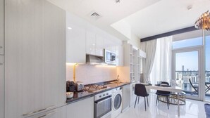 A modern kitchen with a stove, microwave, and washing machine, a dining area with a table and chairs, and a large window offering a city view. - Danube Miraclz 2903 · Breathtaking view compact & modern spacious studio (Arjan)