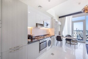 A modern kitchen with a stove, microwave, and washing machine, a dining area with a table and chairs, and a large window offering a city view. - Danube Miraclz 2903 · Breathtaking view compact & modern spacious studio (Arjan)