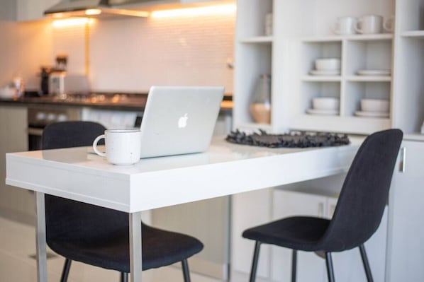 A modern kitchen with a white countertop, a laptop, and a white mug.