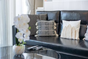 A black leather sofa with patterned cushions, a vase with white flowers, and a remote control on a black table.