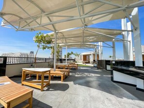 An outdoor patio with wooden tables and chairs, a barbecue grill, and a covered seating area with a view of the city skyline.