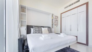 A modern bedroom with a large bed, built-in wardrobe, and a small seating area. - Danube Miraclz 2903 · Breathtaking view compact & modern spacious studio (Arjan)