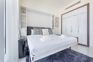 A modern bedroom with a large bed, built-in wardrobe, and a small seating area.