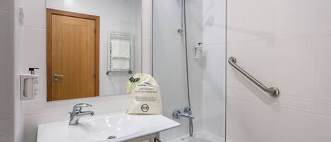 A modern bathroom with a white sink, a wooden door, a glass shower enclosure, and a handrail.