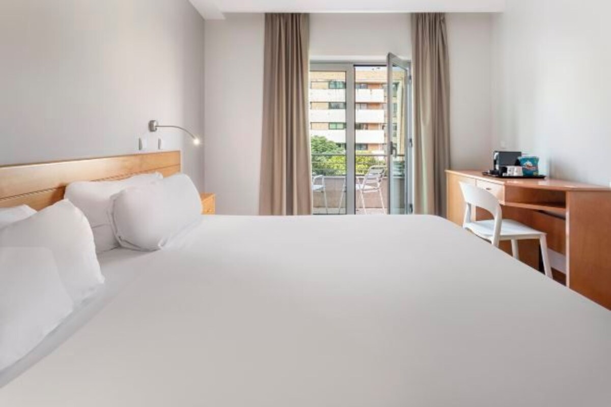 A hotel room with a large bed, a desk, and a view of a balcony.