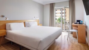Habitación de hotel con una cama grande, cabecera de madera, mesitas de noche, un escritorio con silla y vistas al balcón exterior.