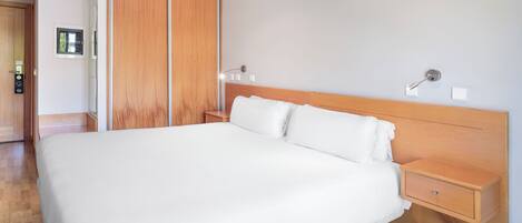 A modern bedroom with a large bed, wooden wardrobe, bedside table, and a small drawer.