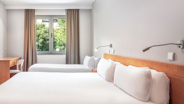 Habitación de hotel con una cama grande, dos mesitas de noche, un escritorio y una ventana con cortinas.
