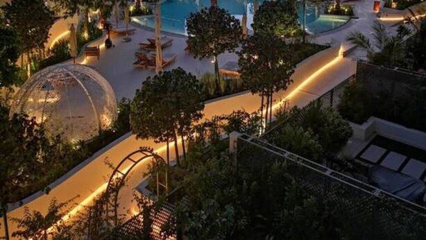 Une piscine sur le toit, agrémentée de palmiers, d’une fontaine circulaire et offrant une vue sur les toits de la ville au crépuscule.