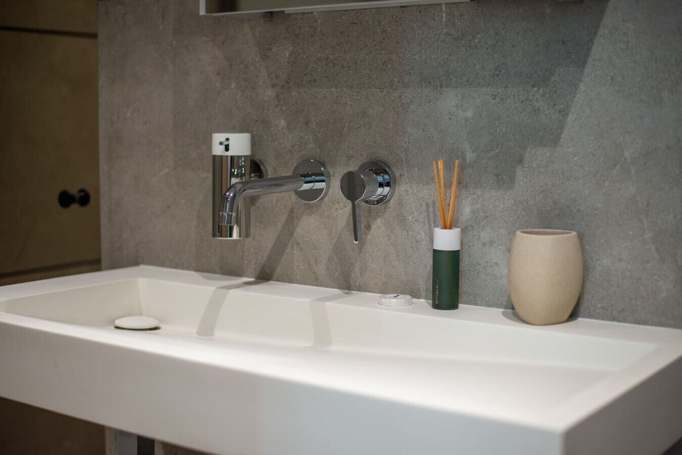 A bathroom sink with a chrome faucet, a soap dish, and a green container with reed diffusers.