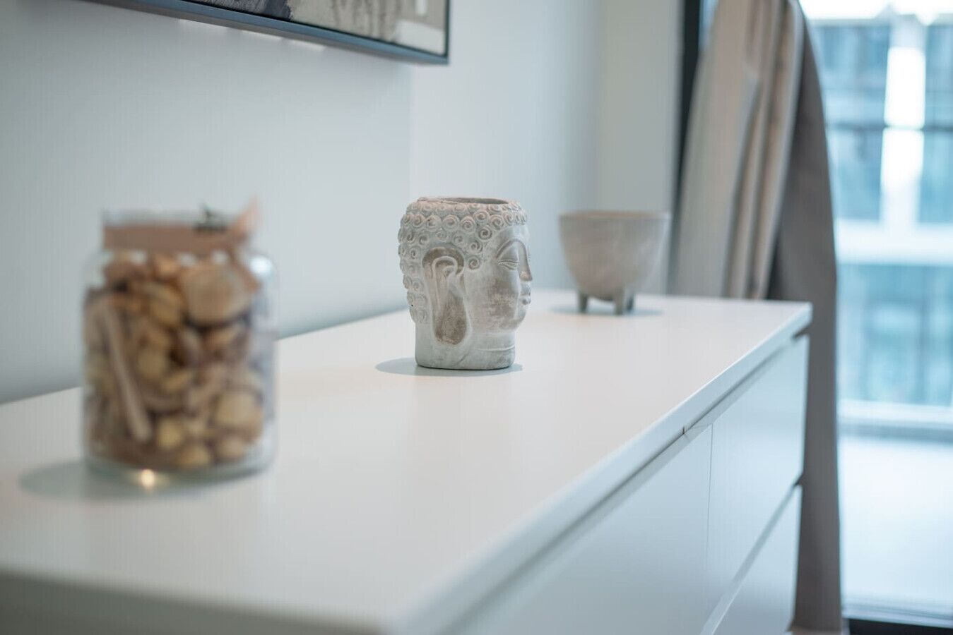 Une table blanche ornée de trois objets décoratifs : un bocal de noix, un vase à visage et un bol.