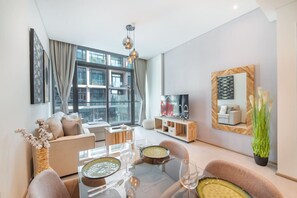 A modern living room with a glass dining table, sofas, a TV, and a large window offering a city view.