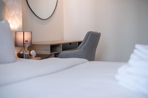 Habitación de hotel con una cama bien hecha, un escritorio con una silla, una lámpara y una botella de agua sobre la mesita de noche.