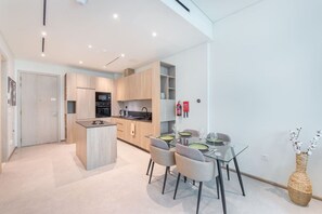 Une cuisine moderne dotée d’appareils électroménagers intégrés, un coin repas avec une table et des chaises en verre, et un petit îlot central.