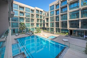 Un bâtiment moderne doté d’une piscine centrale, de nombreux balcons et d’un espace extérieur bien aménagé avec des chaises longues.