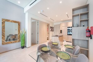 Un espace repas moderne avec une table en verre, des chaises à revêtement gris et un grand miroir au mur.