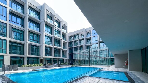 A modern building with a rooftop pool area, featuring a large rectangular pool and a smaller adjacent pool, surrounded by a wooden deck. - JVC-Signature Livings 103 N · Modern flat with KING SIZE bed and HIGH SPEED Wifi (Dubai)