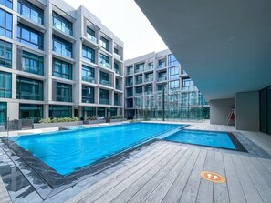 Un bâtiment moderne doté d’une piscine sur le toit, comprenant une grande piscine rectangulaire et une piscine plus petite adjacente, le tout entouré d’une terrasse en bois.