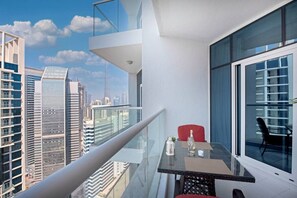 A modern balcony with a glass table, a red chair, and a view of the cityscape. - BUSINESS BAY - Damac Maison prive, 2907 · Spectacular Burj Khalifa view service apartment (Dubai)