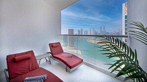 A balcony with two red lounge chairs, a small table, and a view of a city skyline and water body. - BUSINESS BAY - Damac Maison prive, 2907 · Spectacular Burj Khalifa view service apartment (Dubai)