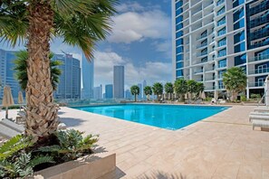 A swimming pool with palm trees, a city skyline, and modern buildings in the background. - BUSINESS BAY - Damac Maison prive, 2907 · Spectacular Burj Khalifa view service apartment (Dubai)